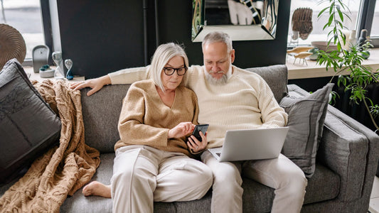 Cuplu de pensionari care cauta oferte turistice pe laptop si telefon
